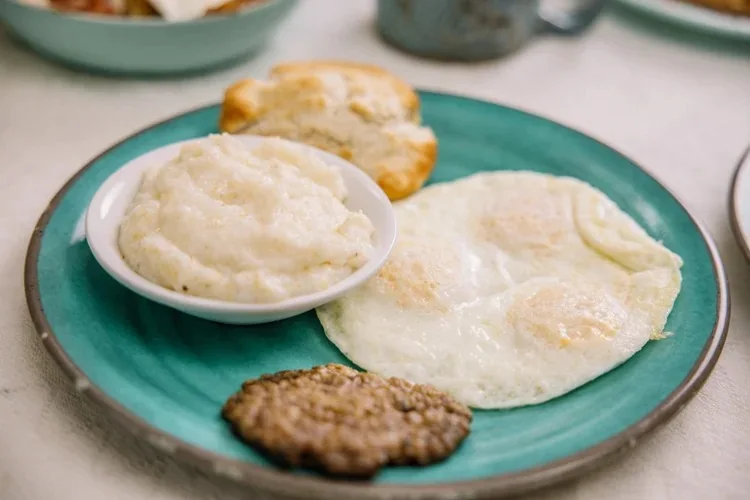 Grits, eggs, biscuit and sausage on a teal plate